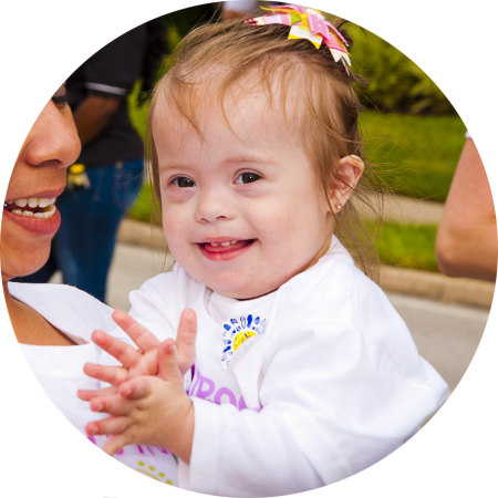 Smiling down syndrome child wearing a bow in her hair and white top