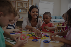 Un adulte et 5 petits enfants jouent assis autour d'une table.