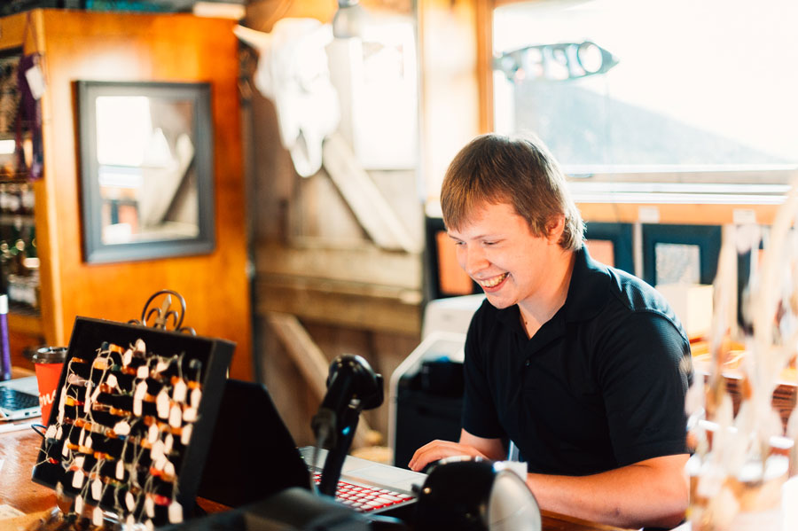 A smiling young adult man working at a cash register in a retail store.
