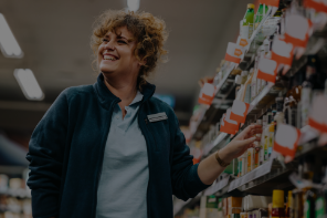 A woman wearing a name tag and looking at the aisles of products in a grocery store.