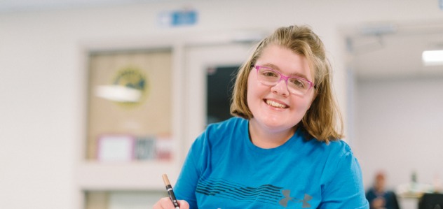 Une jeune femme souriante portant des lunettes roses et une chemise bleue.