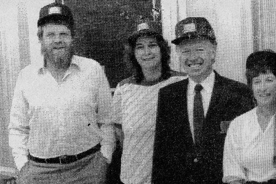 Two men and a woman wearing matching baseball caps