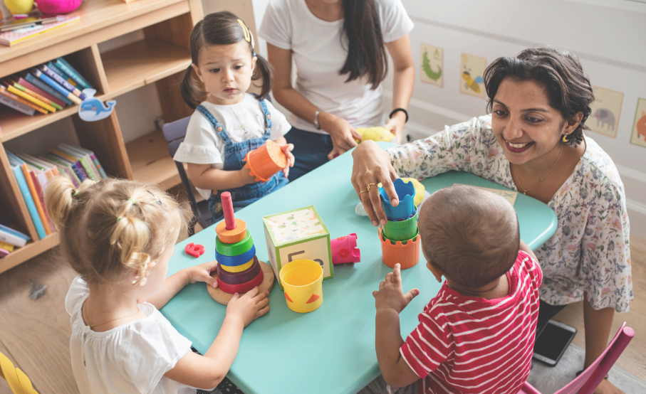 Deux femmes et trois enfants réunis autour d’une petite table avec des jouets colorés.